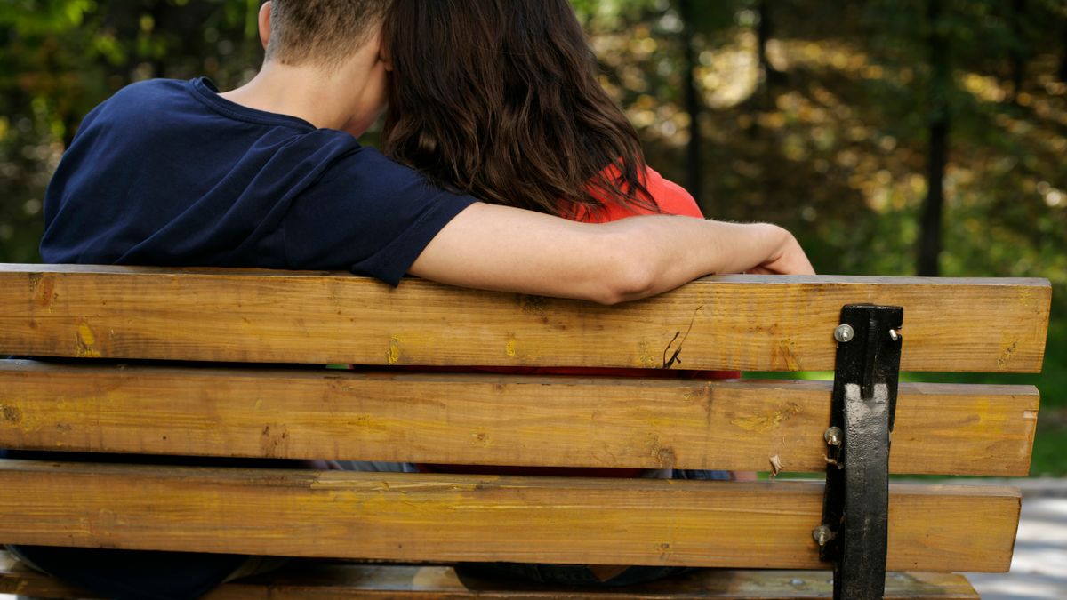 A couple sitting close together on a park bench, seen from behind
